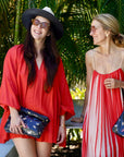 Two women in red outfits with black butterfly bags standing outdoors with palm trees in the background