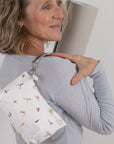 Woman holding a yoga mat with a white pouch featuring people doing yoga on her shoulder.