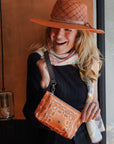 Woman wearing an orange hat and holding an orange bandana patterned bag indoors.