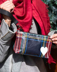 Hand holding zip wristlet in tartan plaid with red scarf and gray jacket in the background.