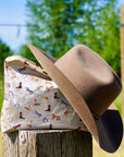 Shimmer beige equestrian pattern zipper pouch sitting on tree stump with cowboy hat