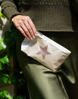 Woman in olive green dress holding mini zipper pouch in shimmer beige with bronze star