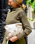 Woman in olive green sweater holding a medium shimmer beige clutch with multi bronze stars