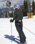Skier wearing the black puffer sling backpack with gold heart on a snowy slope beside a gondola lift