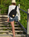 Woman in a straw hat wearing the black puffer sling backpack with gold heart on wooden beach stairs