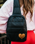 Black puffer crossbody backpack with gold heart worn across the back over a ski jacket