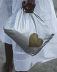 Person in dress on sand holding medium zipper pouch in silver with gold heart
