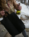 Woman pulling a wine bottle out of side pocket of black wine tote bag