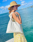 Woman in a yellow dress and hat holding shimmer white puffer tote over shoulder
