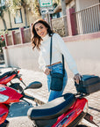 Woman in white sweater standing alongside red scooter wearing crossbody shimmer black cell phone purse