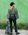 Woman standing in front of green wall wearing Puffer Crossbody Fanny Pack Belt Bag in Shimmer Black
