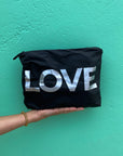 Hand holding the Medium Pouch in Black with Silver LOVE against a bright teal wall