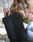 Woman pulling a wine bottle out of side pocket of black wine tote bag