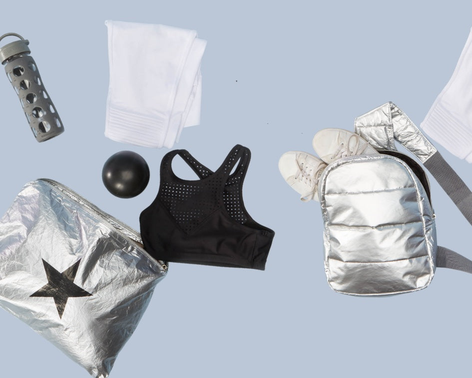 Silver crossbody backpack, silver jumbo pouch with black star, and various gym items on blue background