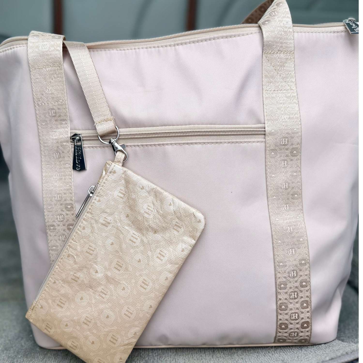 A light beige nylon tote bag with beige woven trim and a matching beige patterned zippered pouch, shown on a neutral gray background.
