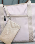 A light beige nylon tote bag with beige woven trim and a matching beige patterned zippered pouch, shown on a neutral gray background.
