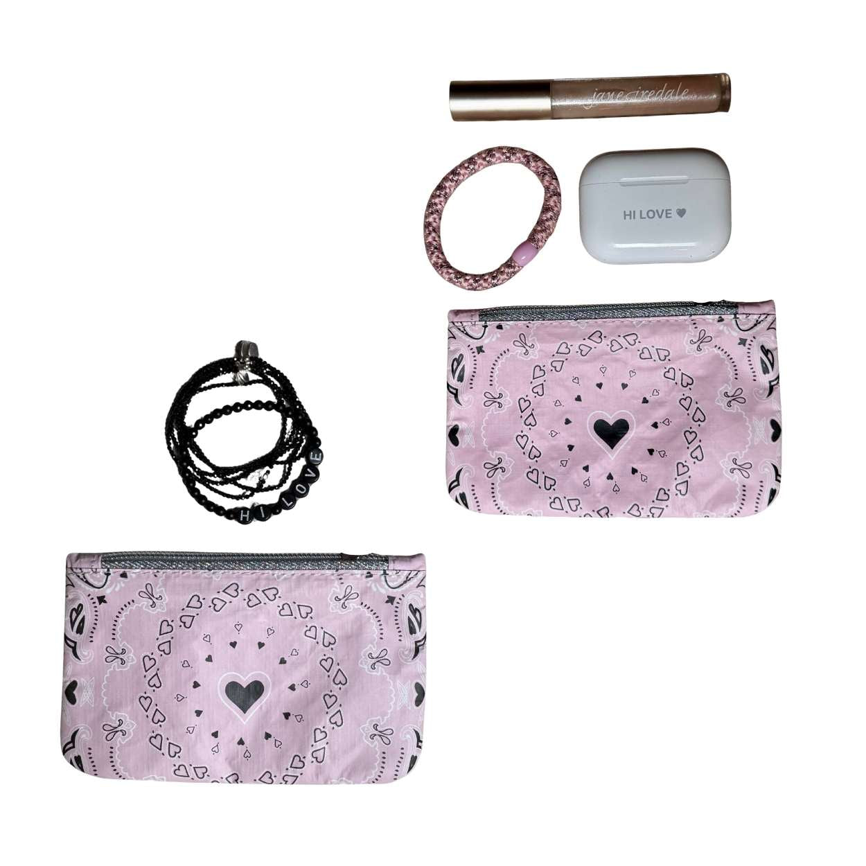 Little zipper pouches in a pink heart pattern Bandana Print storing lip gloss, hair tie, bracelets and ear pods on a white background.