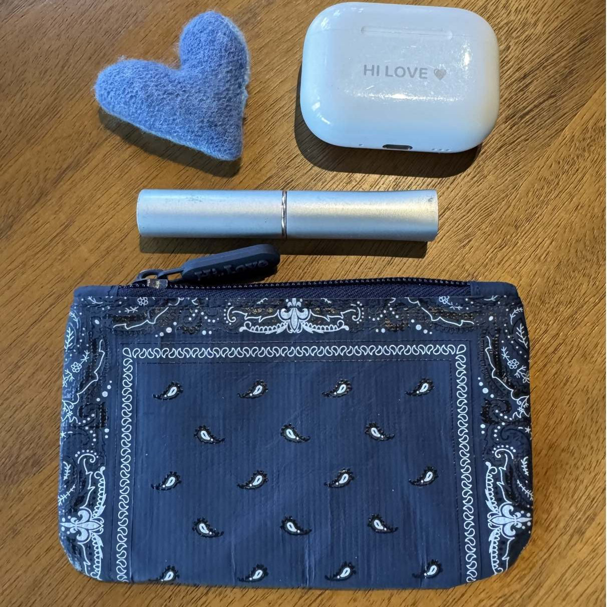 Blue patterned pouch with a cashmere, ear buds, and lip balm on a wooden surface.