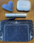Blue patterned pouch with a cashmere, ear buds, and lip balm on a wooden surface.