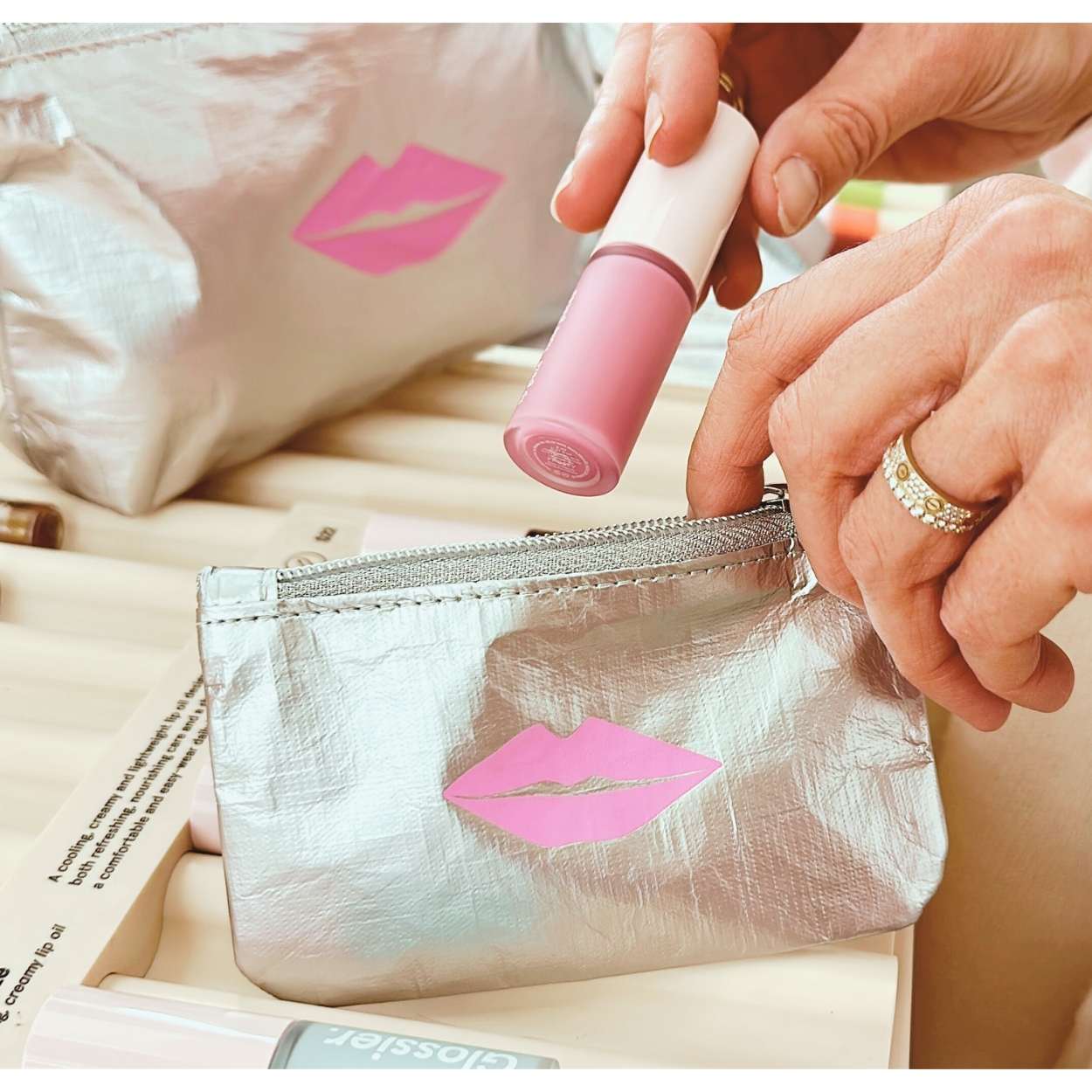 Person placing lip gloss in a silver makeup bag with pink lip design.