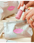 Person placing lip gloss in a silver makeup bag with pink lip design.