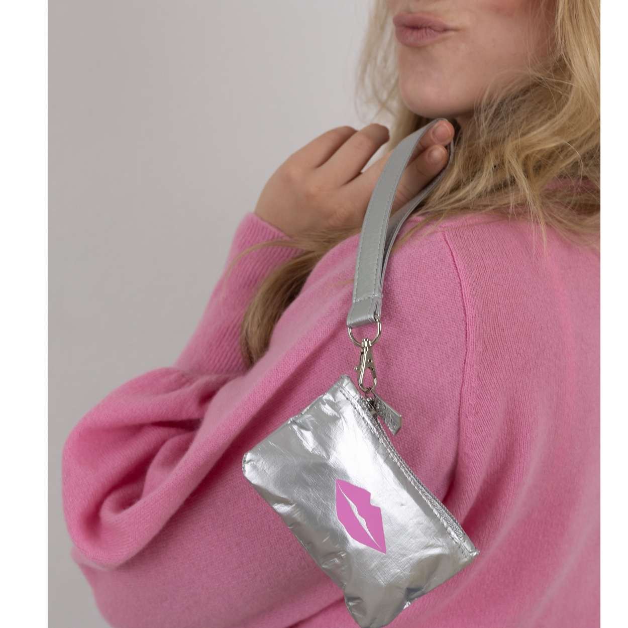 Person wearing a silver wristlet pouch with a pink lip design on a plain background