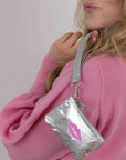 Person wearing a silver wristlet pouch with a pink lip design on a plain background