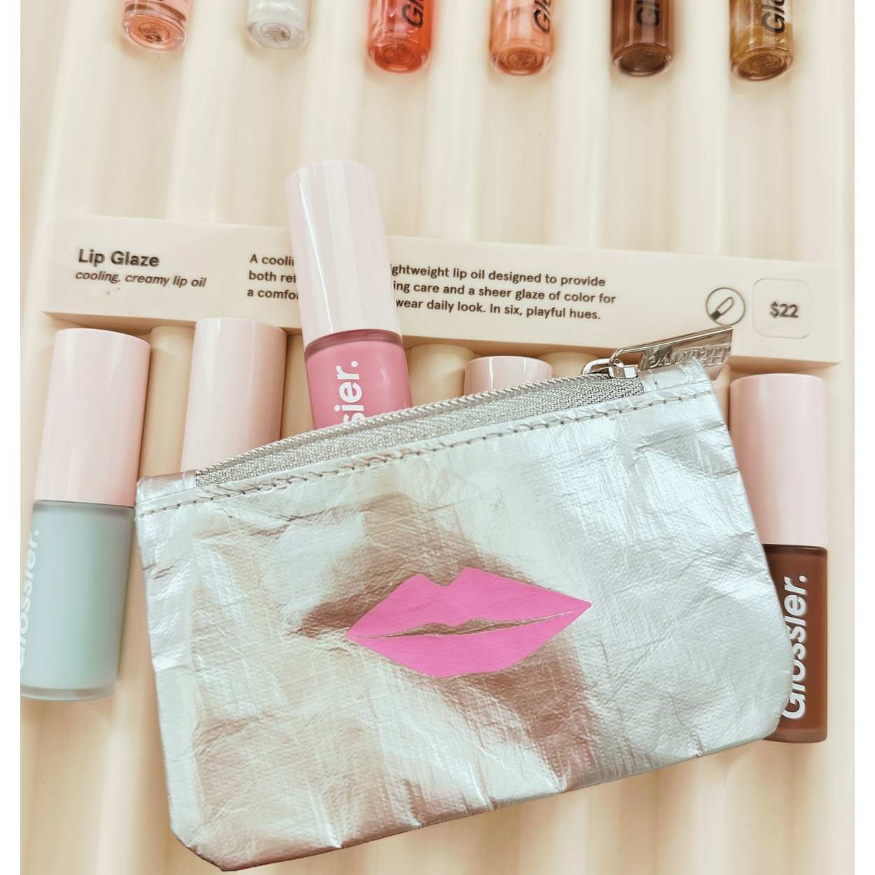 Makeup products including lip glosses and a pouch with pink lips design on a beige background.