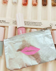 Makeup products including lip glosses and a pouch with pink lips design on a beige background.