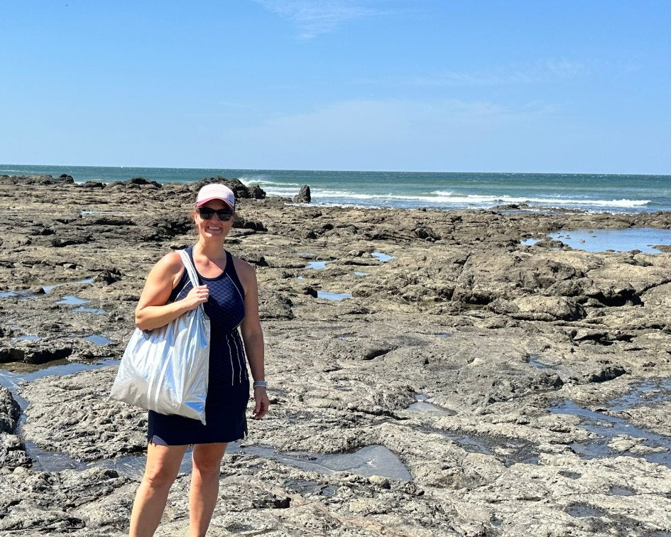 Woman wearing navy top and skirt carrying carryall tote bag in silver with white stripes on beach in Tamarindo Costa Rica 