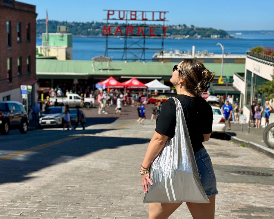 Woman walking around Pike Place Market in Seattle carrying carryall tote bag in silver with white stripes