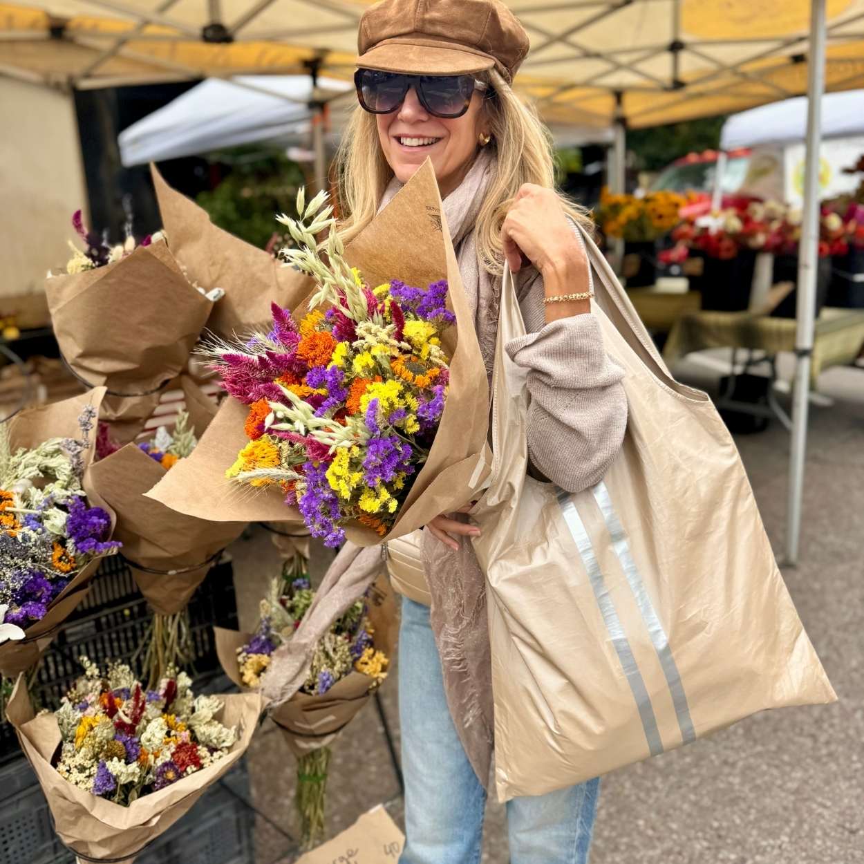 Woman holding flowers and carryall tote in shimmer beige with silver stripes at farmers market