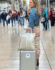 Woman with a suitcase and striped beige tote bag shopping along a busy city street