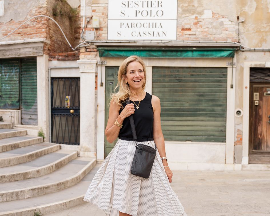 Woman in black top and white skirt walking in an urban setting wearing a shimmer black cell phone purse.
