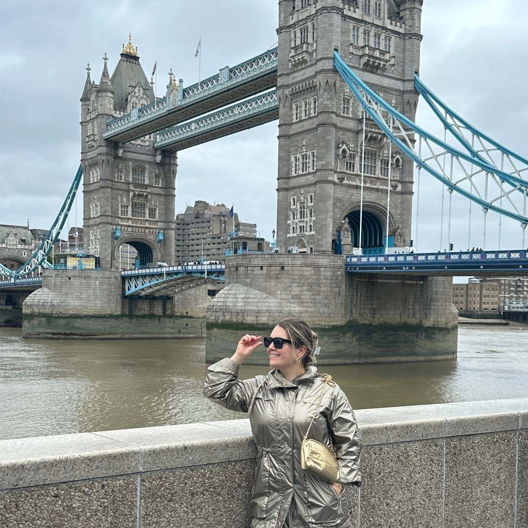 Woman in a metallic jacket standing in front of Tower Bridge, London with a gold chain purse
