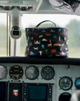 A black travel-themed lunch case with a colorful cartoon print sits on the dashboard of an airplane cockpit.