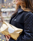 Woman wearing black jacket holding cosmetic zipper pouch gold with silver heart 