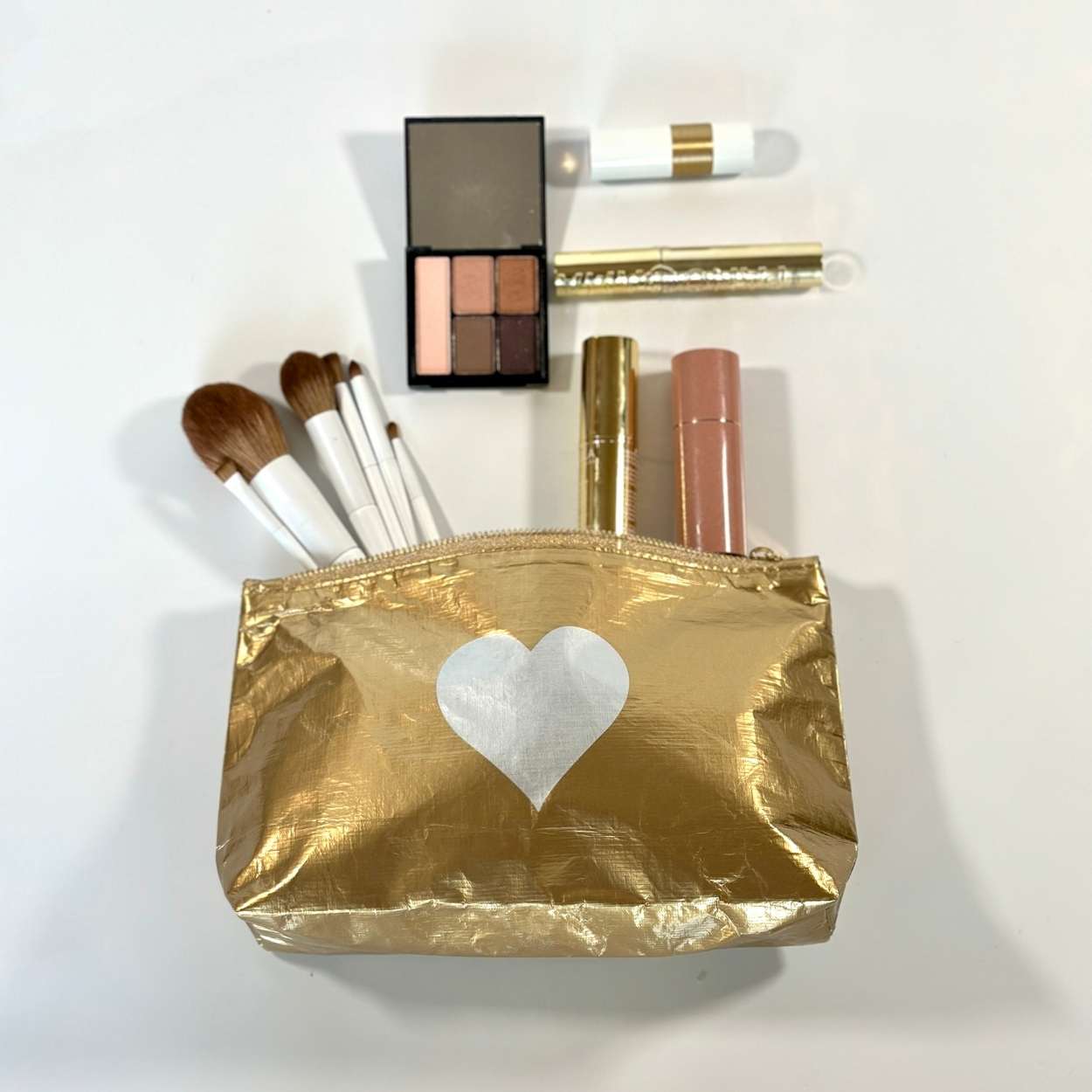 Cosmetic zipper pouch gold with silver heart containing makeup on white background