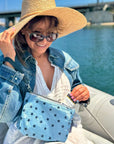 Woman on boat grabbing sunscreen from cosmetic zipper pouch light blue shimmer myriad stars with detachable navy wristlet strap