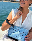 Woman on boat holding cosmetic zipper pouch light blue shimmer myriad stars with detachable navy wristlet strap