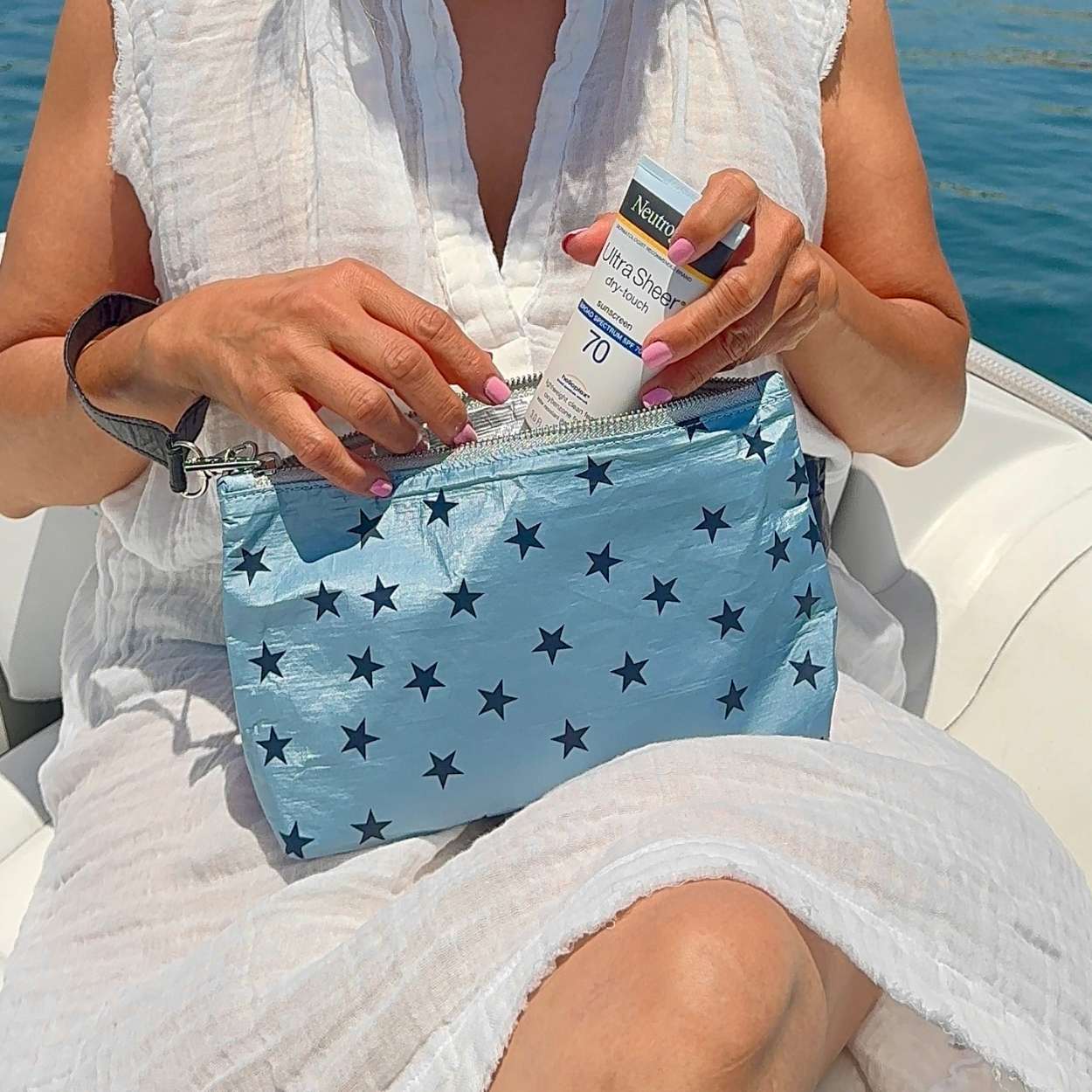 Person grabbing sunscreen from cosmetic zipper pouch light blue shimmer myriad stars