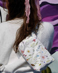 Woman holding cosmetic zipper pouch in spring wildflowers with butterflies