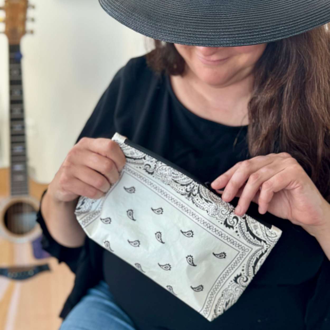 Woman in black hat holding cosmetic zipper pouch in white bandana print