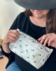 Woman in black hat holding cosmetic zipper pouch in white bandana print