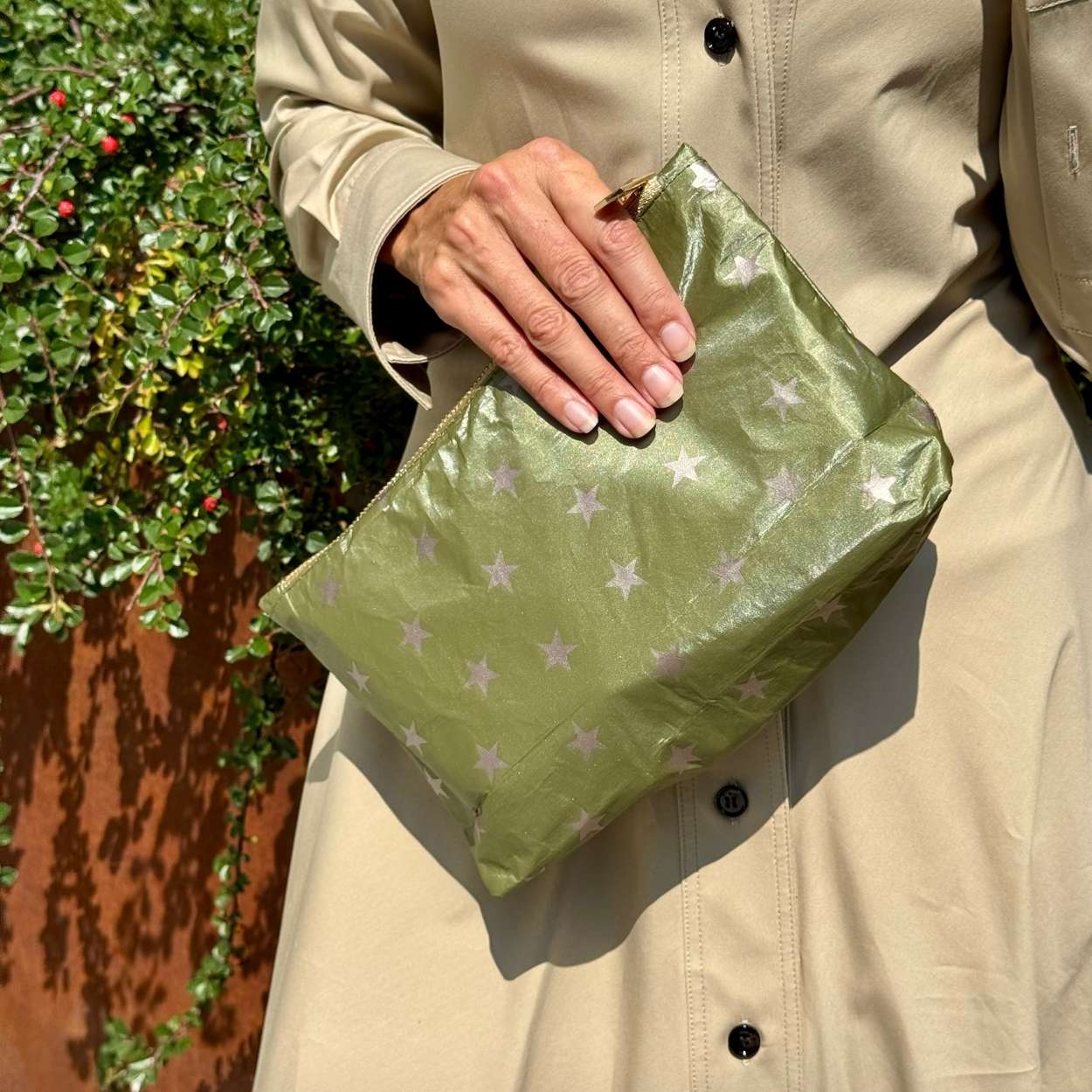 Person holding an olive green fabric pouch with star pattern against a natural background