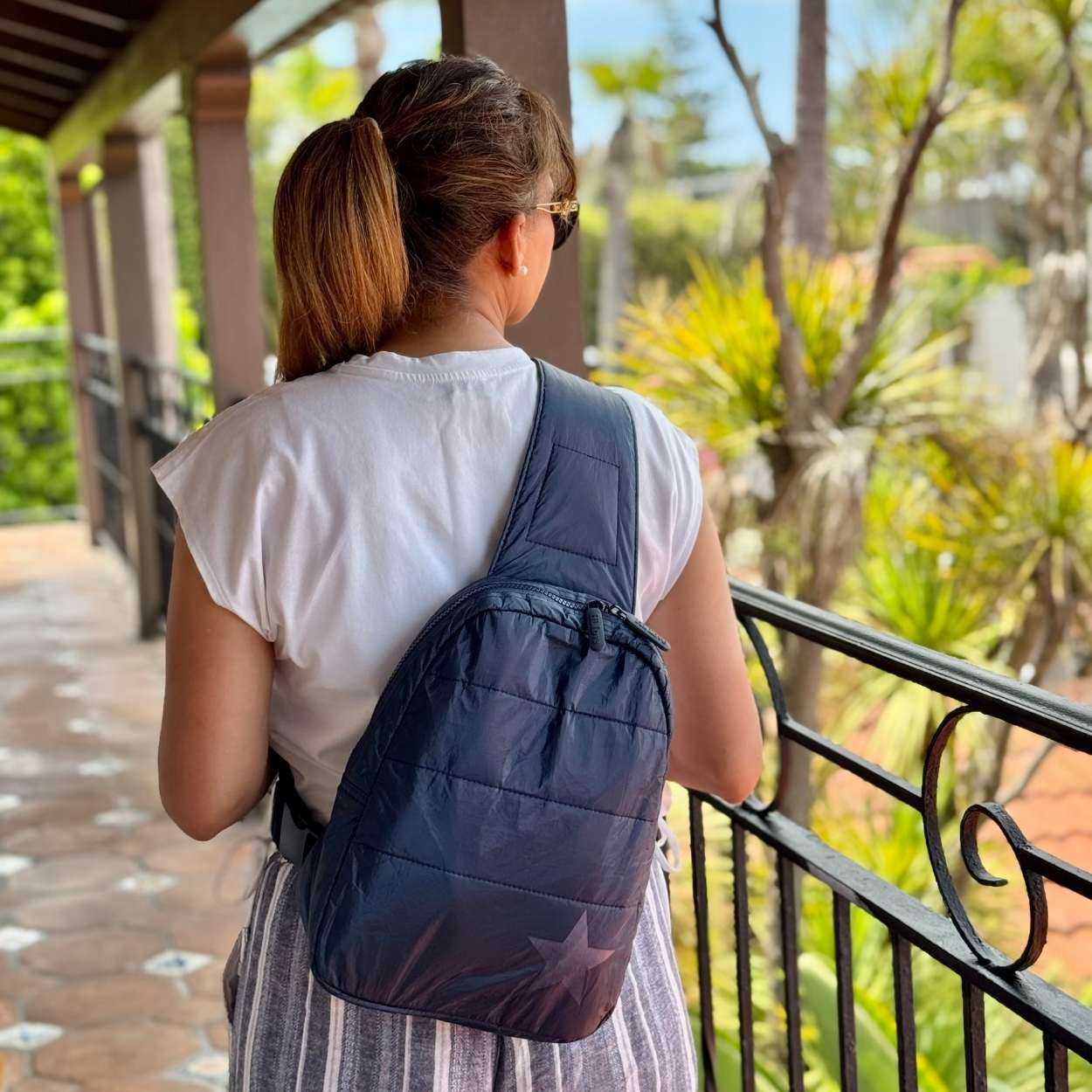 Woman in tropical area holding crossbody backpack in shimmer navy with tonal star