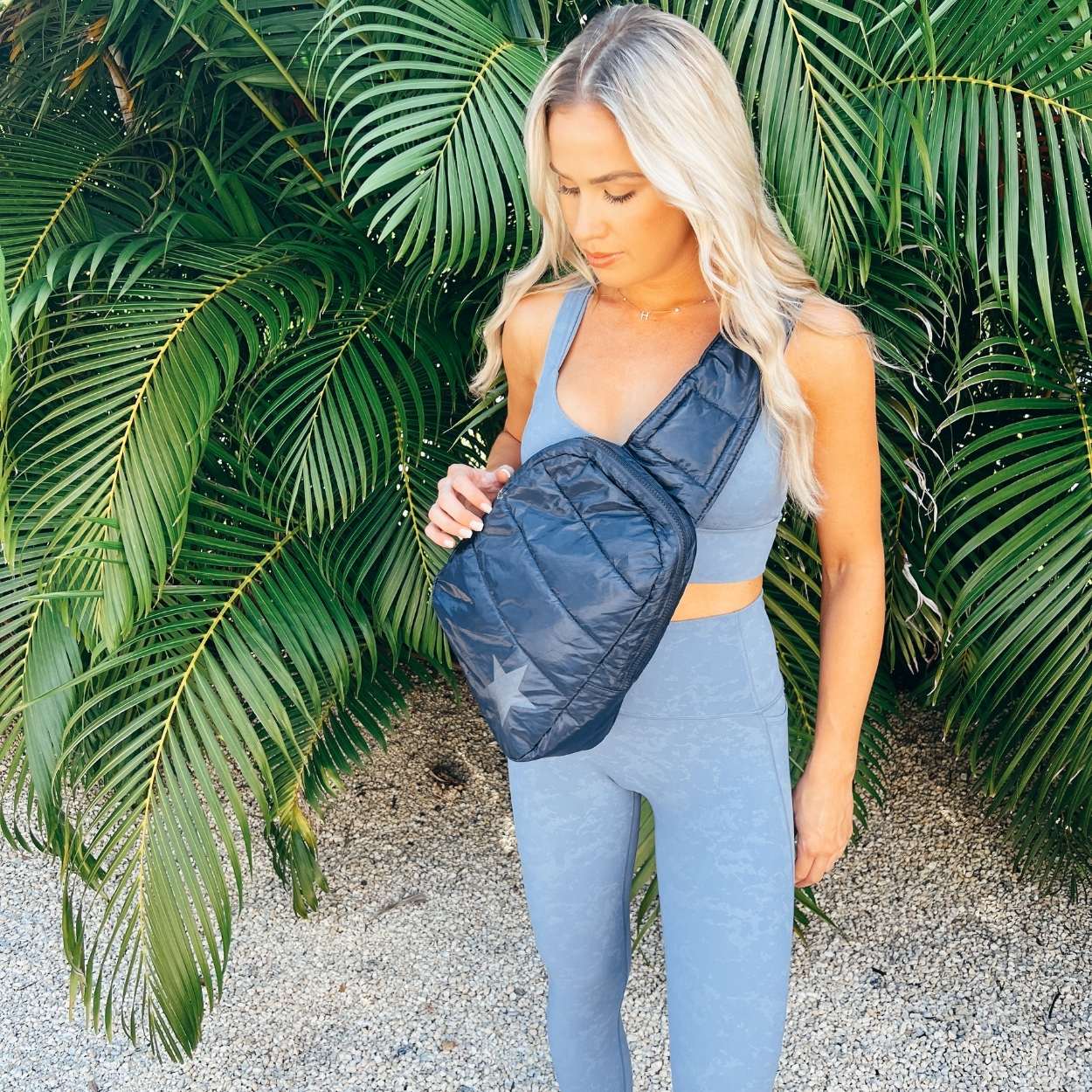 Woman in workout set with crossbody backpack in shimmer navy with tonal star on palm tree background