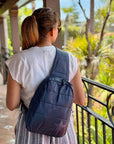 Woman in tropical area holding crossbody backpack in shimmer navy with tonal star