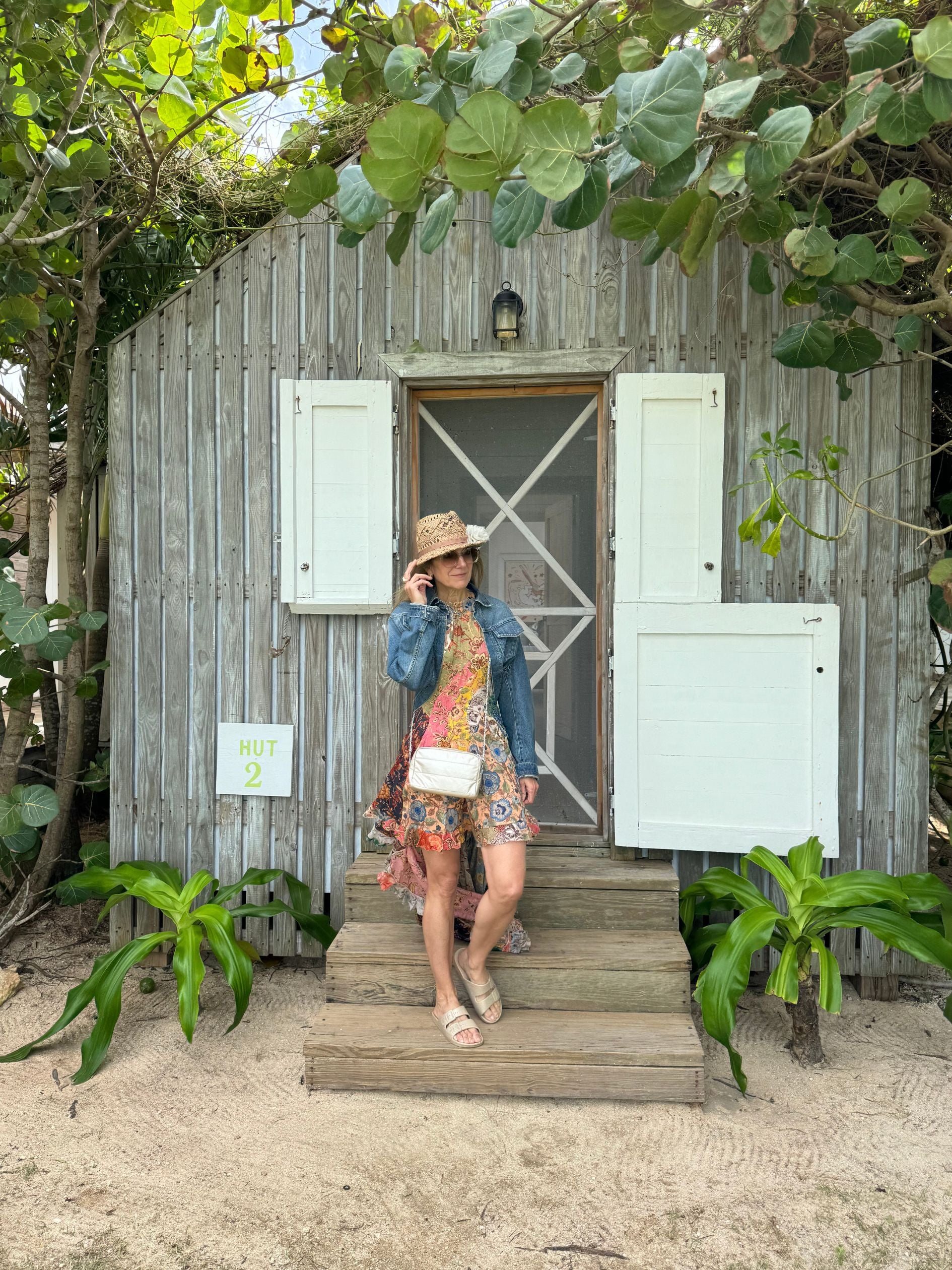 Woman walking out of The Other Side Hotel hut in the Bahamas wearing sundress, sunhat, and mimi puffer chain bag