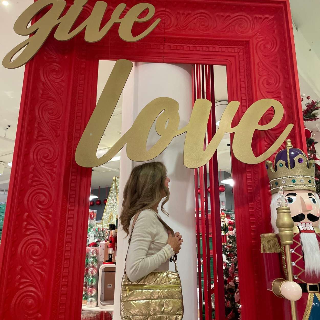 Woman holding crossbody puffer purse in gold with give love holiday background